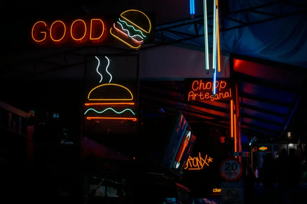 Papan neon berwarna cerah di pasar malam kota menampilkan iklan burger dan minuman, menggambarkan contoh kata kata iklan makanan yang menarik